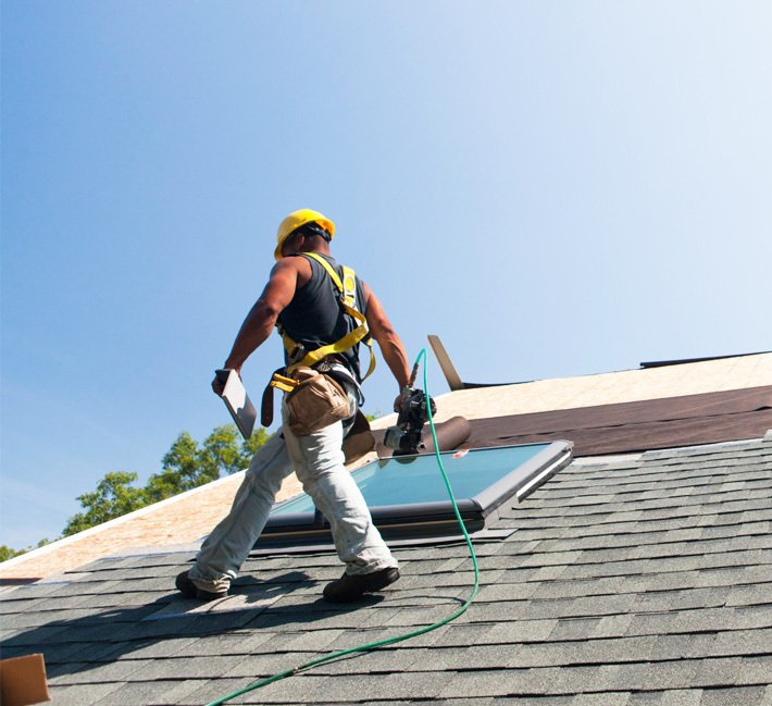 Man walking on roof laying asphalt shingles.