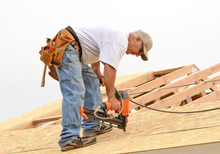 Man on roof with nail gun nailing particle board to new roof.