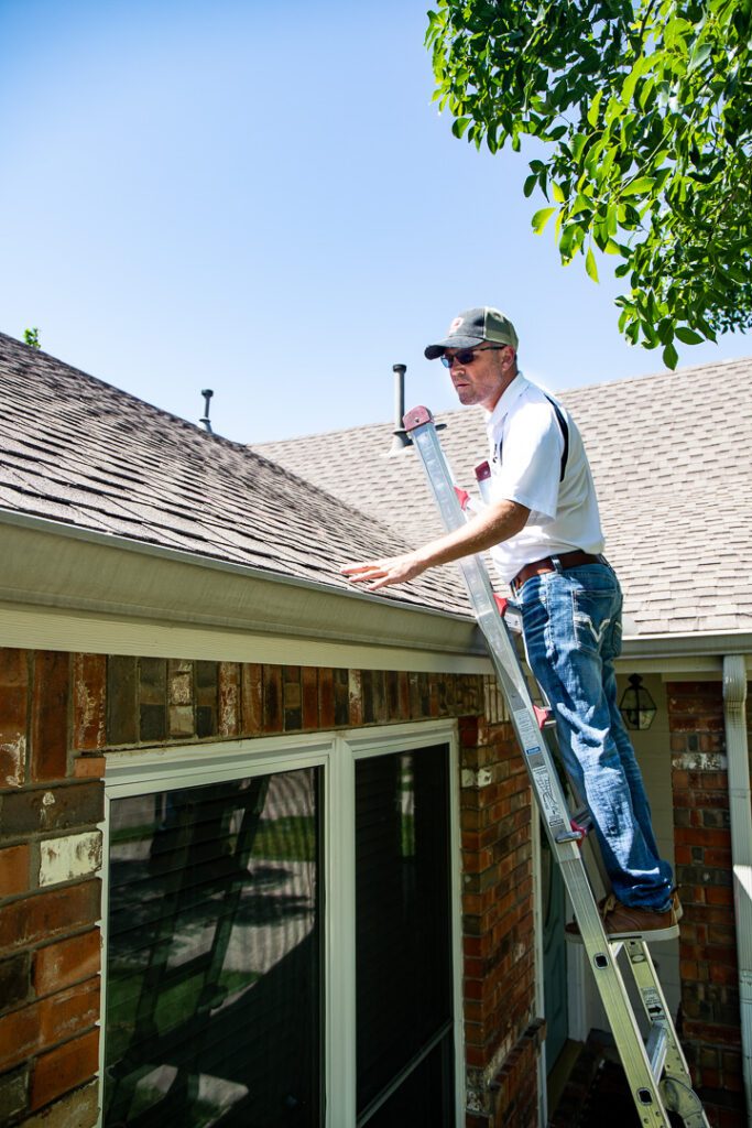 Tony, Owner of Lake Dallas Roofing and Restorations, on a ladder looking at an asphalt shingled roof