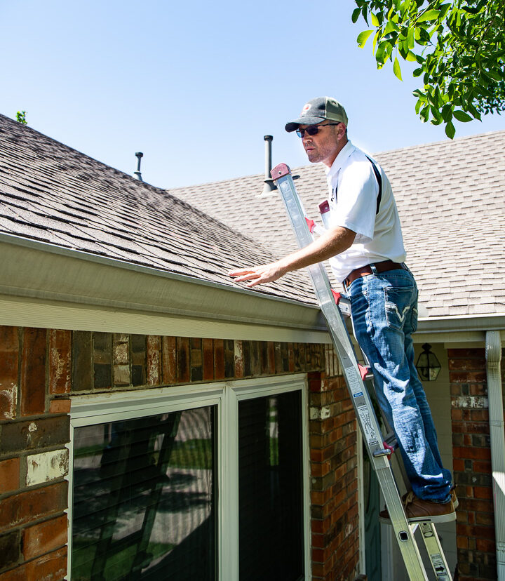 Tony, Owner of Lake Dallas Roofing and Restorations, on a ladder looking at an asphalt shingled roof