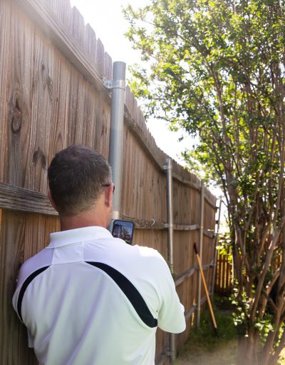 Tony, owner of Lake Dallas Roofing & Restorations, examining a residential wooden fence that's out of alignment.